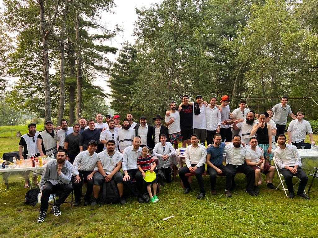 A large group of talmidim posing outdoors at a barbecue among the trees