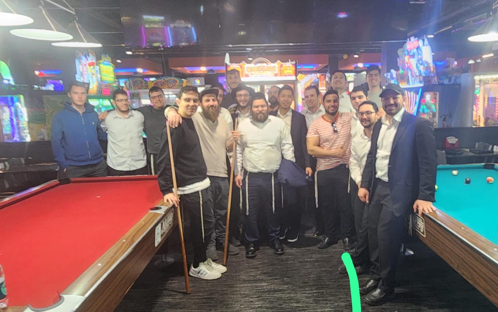 Talmidim posing together with cues between two pool tables