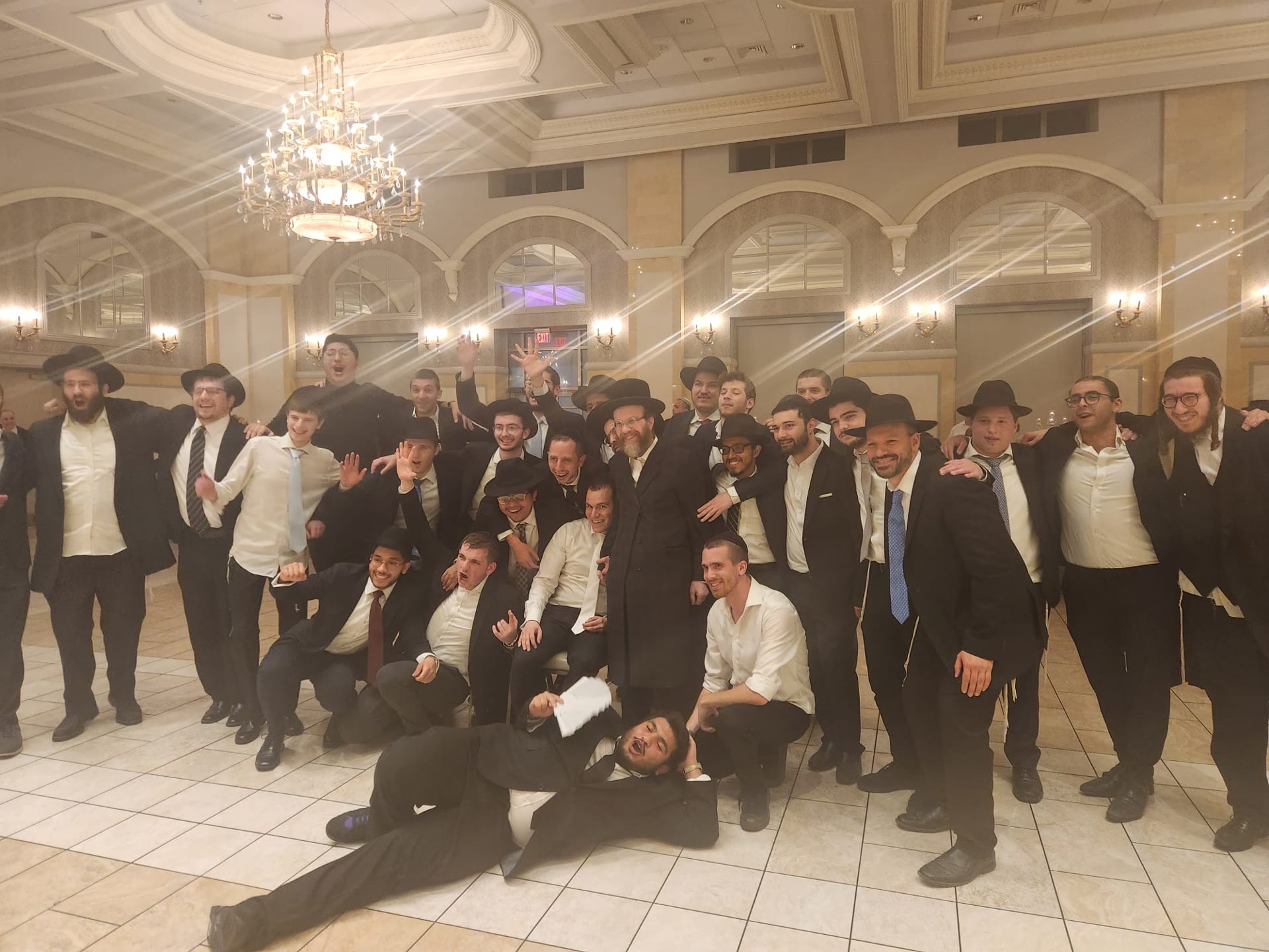 A large group of talmidim celebrating with a rebbe in a ballroom