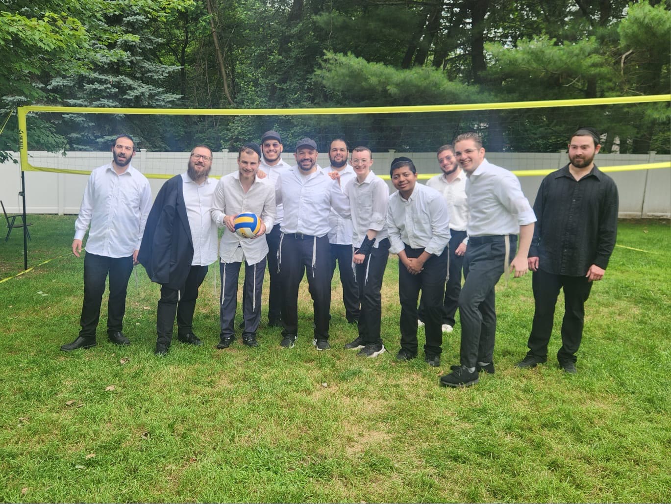 Talmidim posing with a volleyball in front of the net outdoors