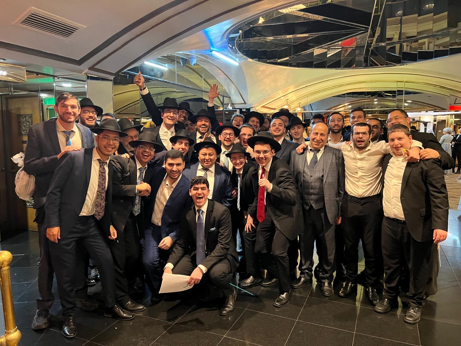 Talmidim and rebbeim posing together in a hall lobby after a simcha
