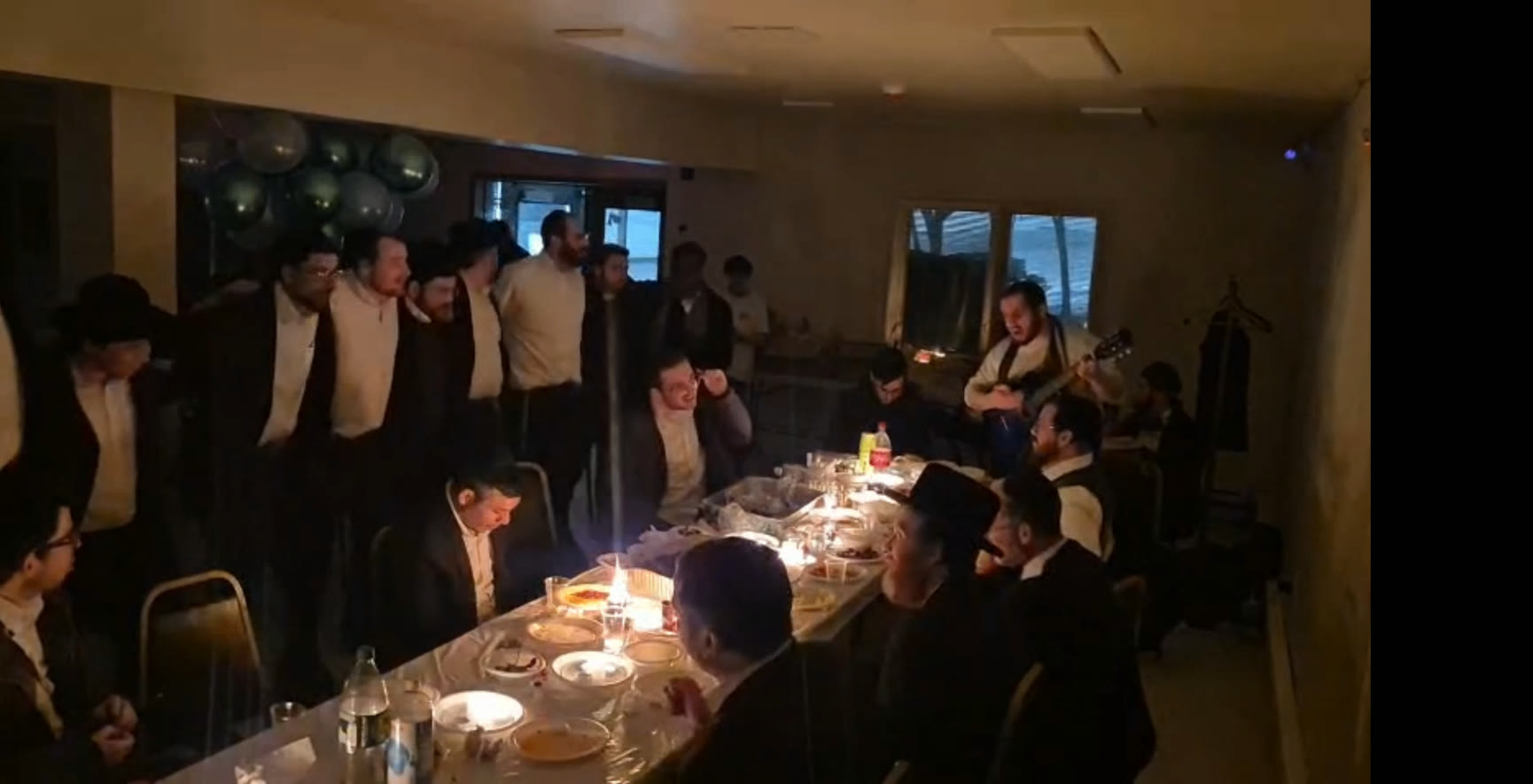 Talmidim singing together around a long table with a guitar