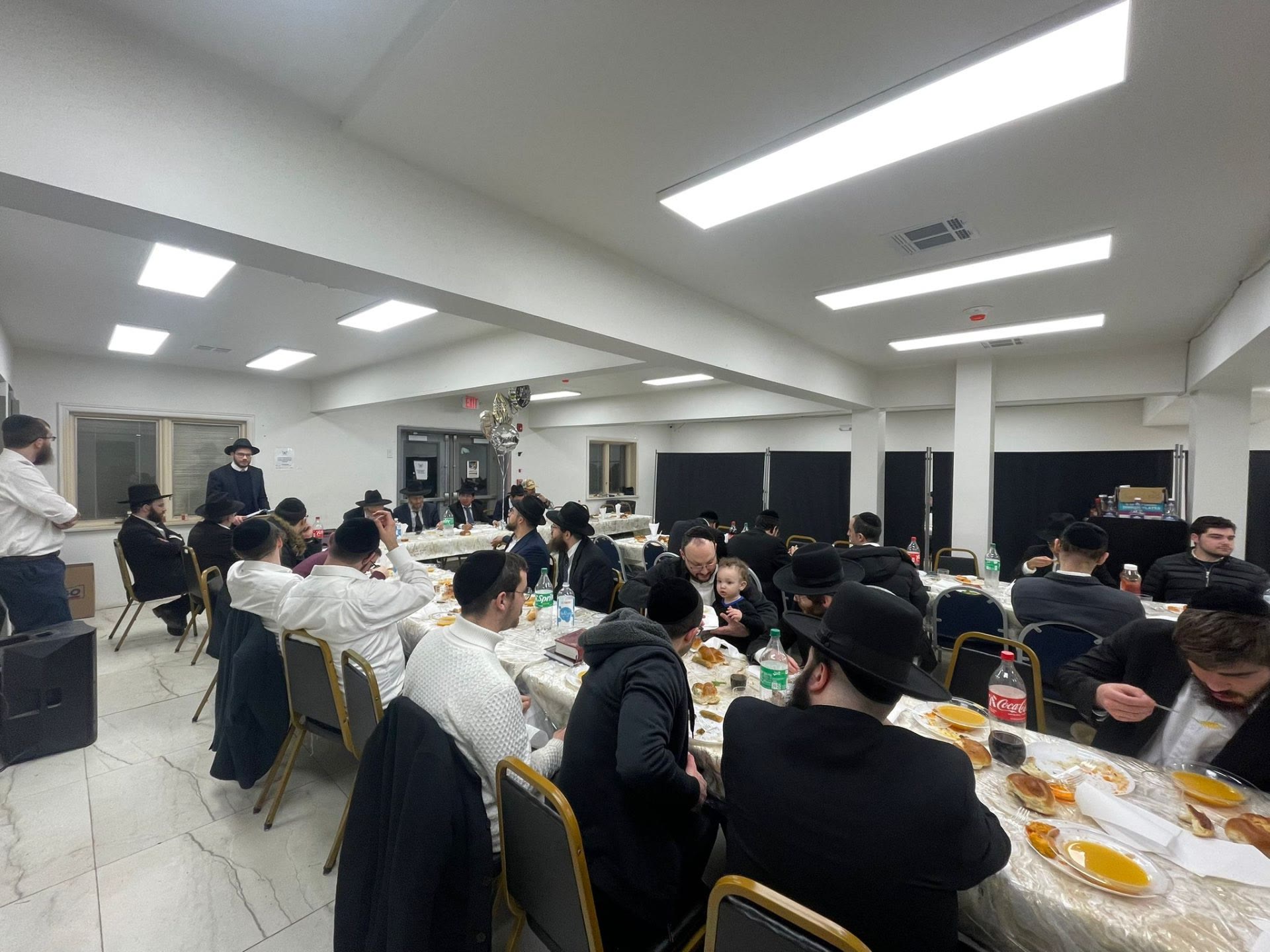 Talmidim and families eating together at long tables in the hall