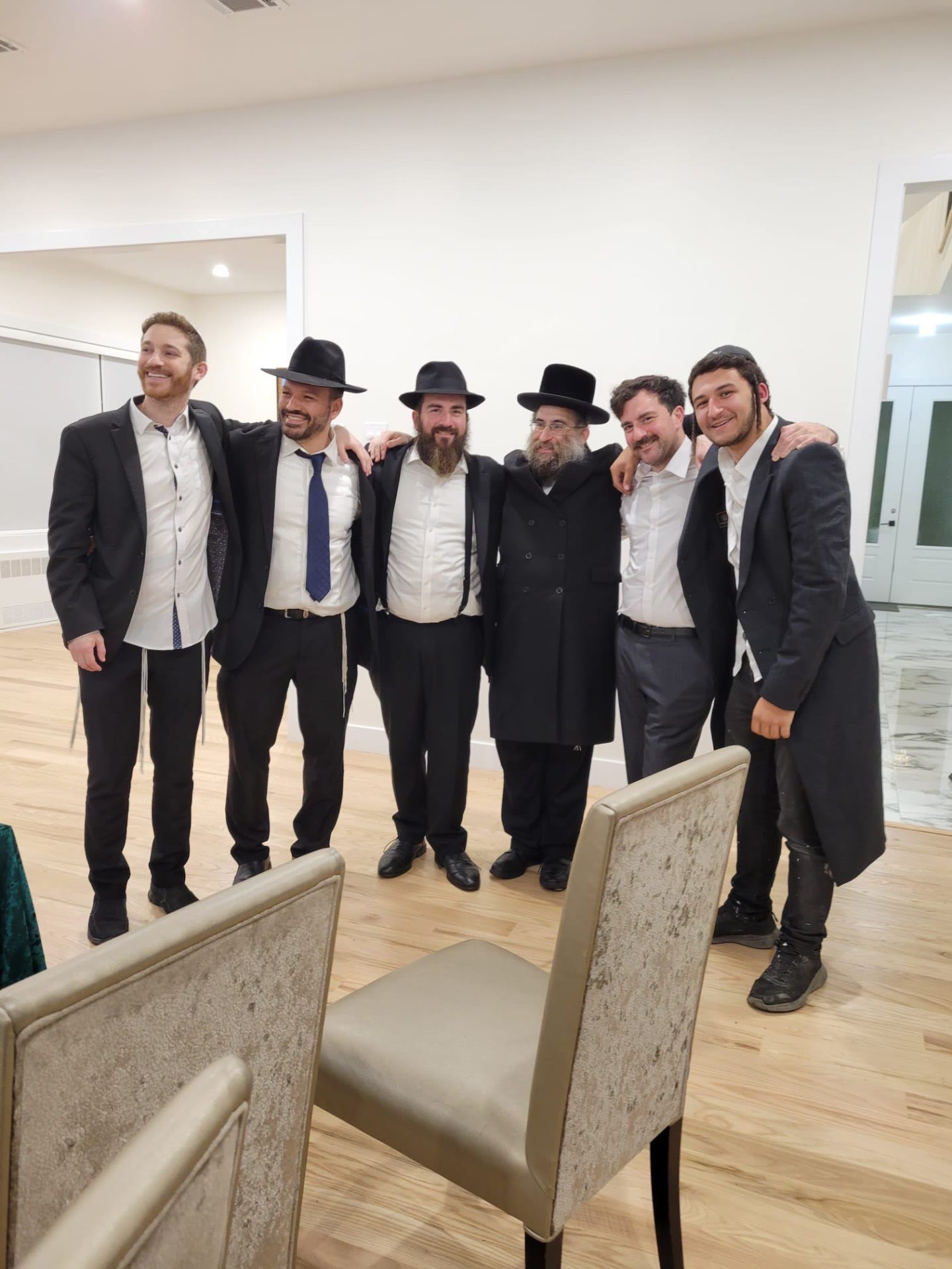 Talmidim standing arm in arm with a rebbe at a simcha