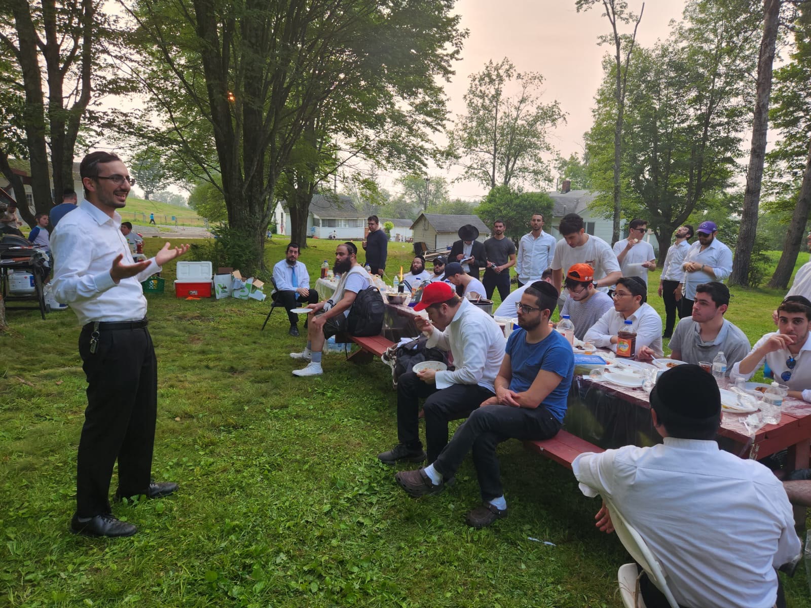 A speaker addressing talmidim seated at picnic tables outdoors