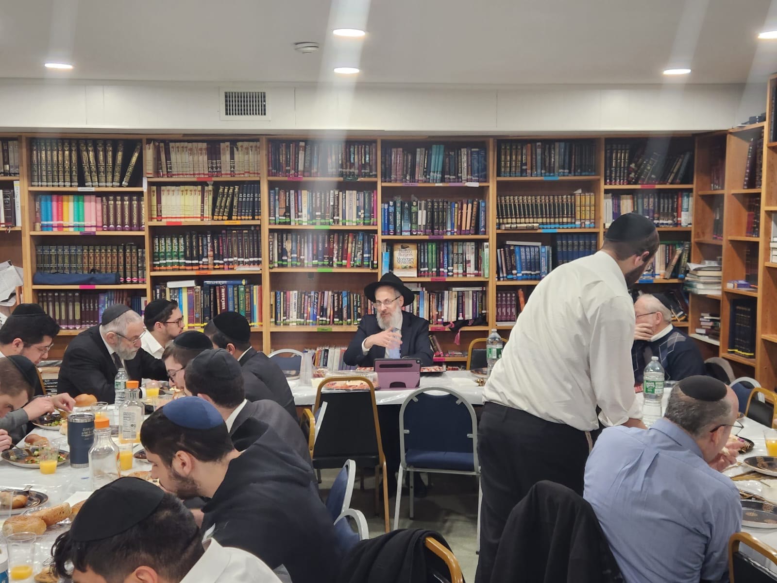 Talmidim and rebbeim eating together surrounded by seforim shelves