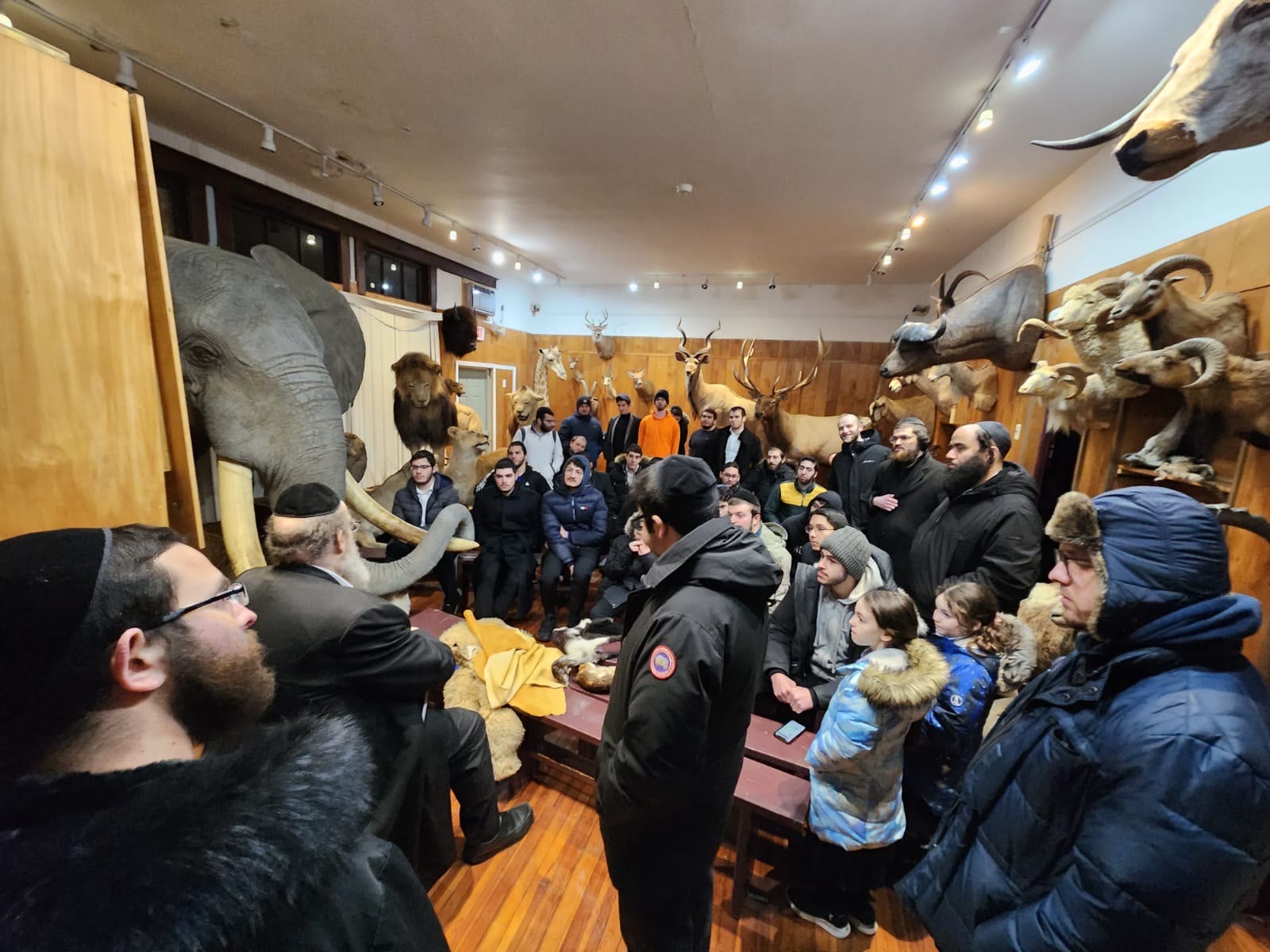 Talmidim gathered listening to a presentation in a room of animal exhibits