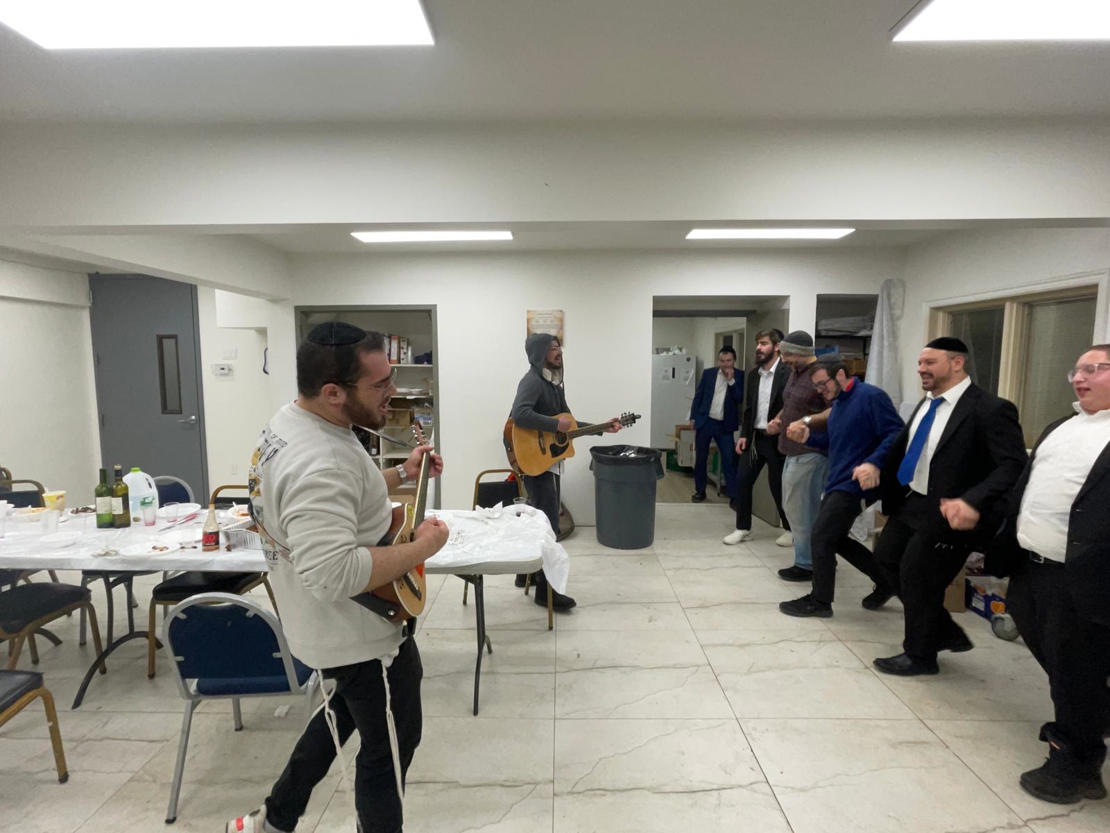 Two guitarists playing while talmidim dance in the hall