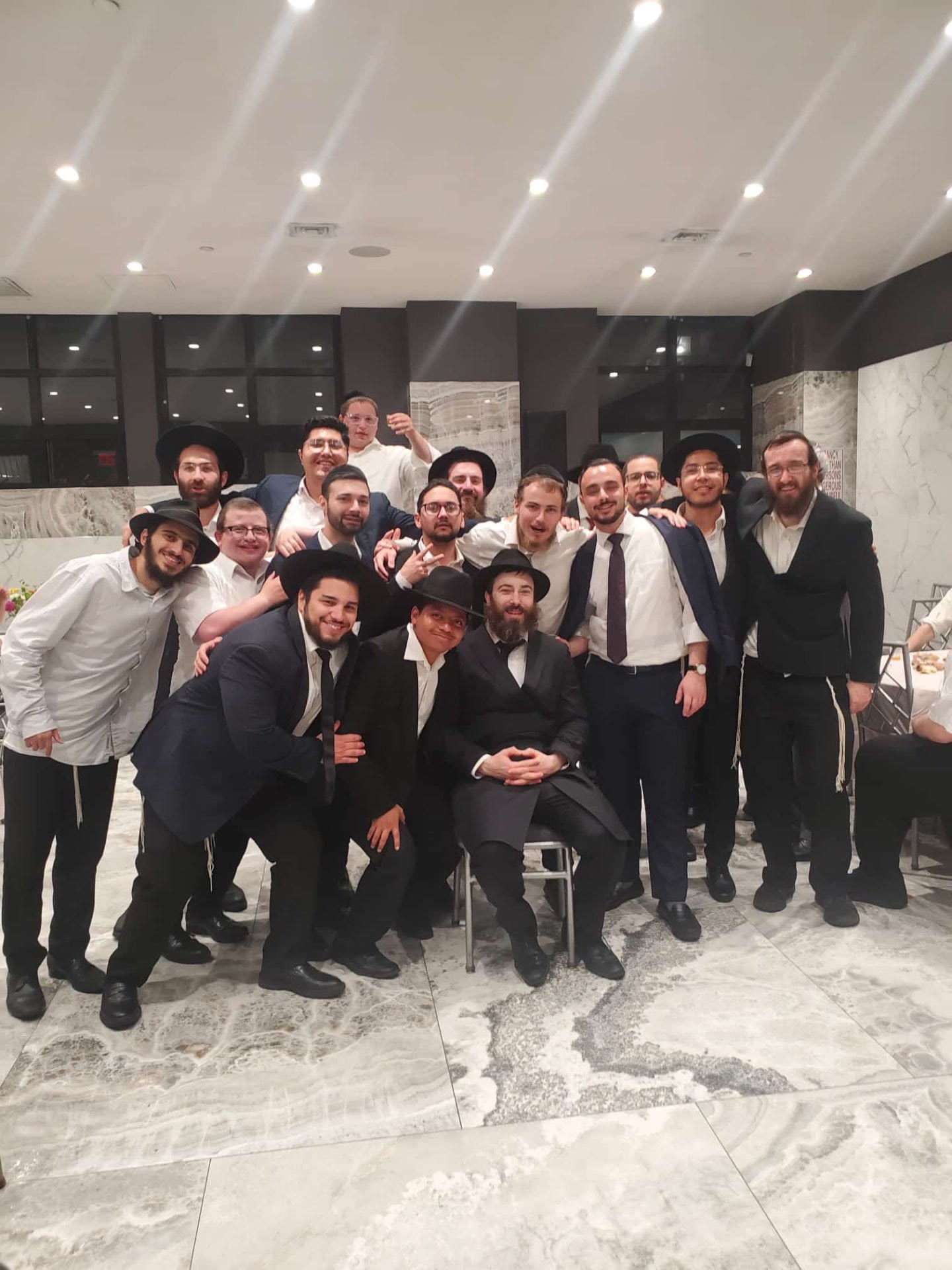 Talmidim gathered around a rebbe at a wedding hall